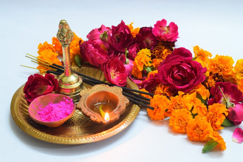 A tray carrying flowers, incense and lit oil candle in a small clay container.