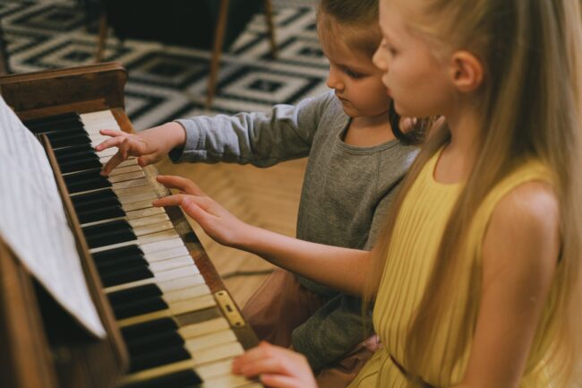 Two kids sitting at a piano playing the keys.