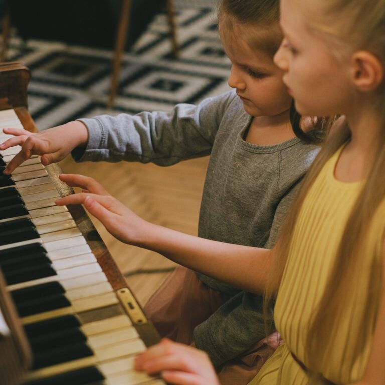 Two kids sitting at a piano playing the keys.