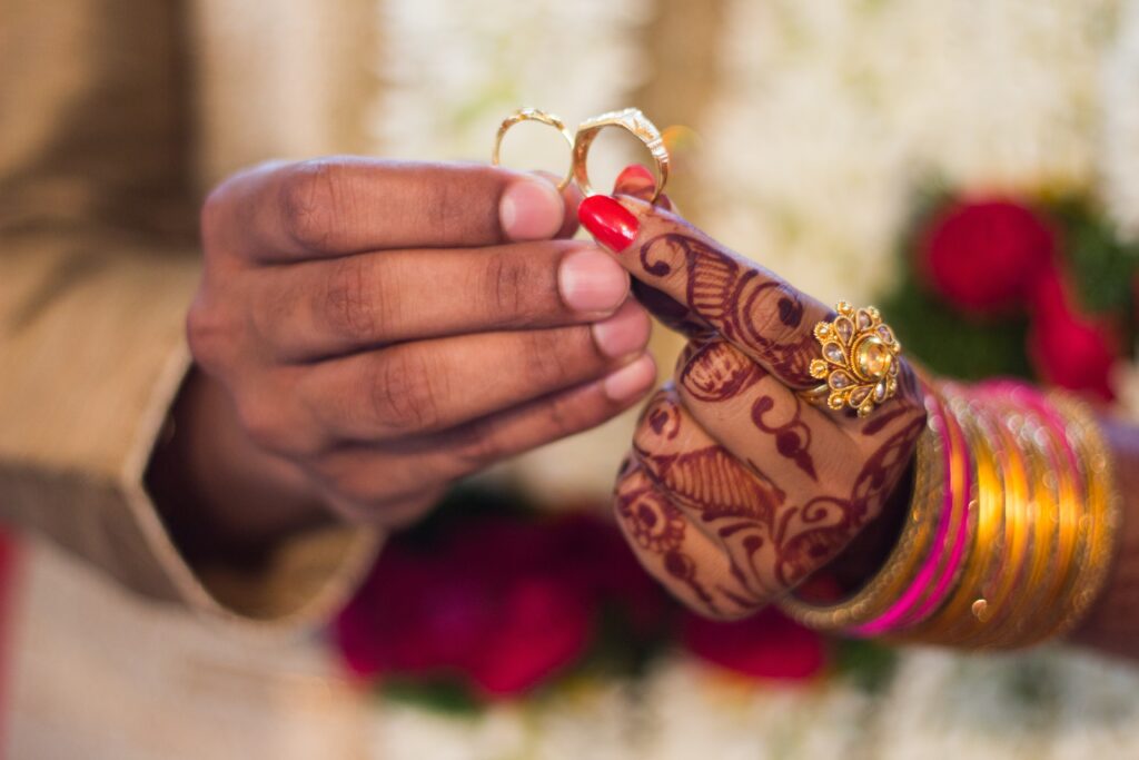 Two hands holding wedding rings. One hand is decorated with henna.