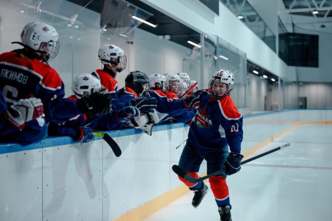 Hockey player skating along side bench and fist bumping teammates
