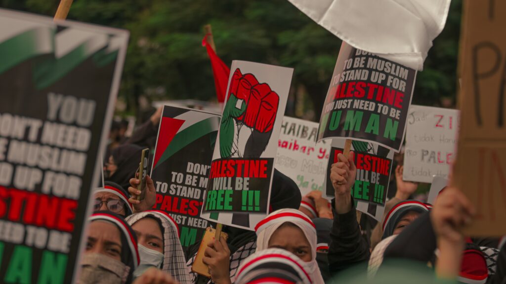 protesters holding poster reading "Palestine will be free" in red, green, white font.