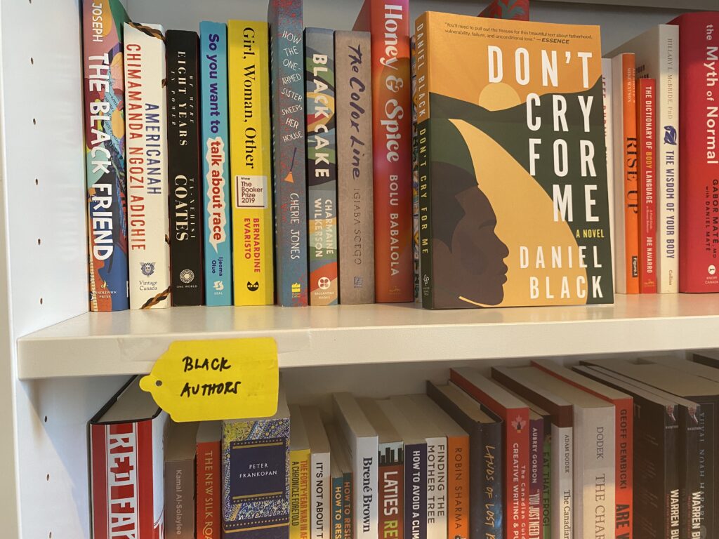A yellow label saying Black authors sits on a bookshelf. On the shelf is a number of novels.