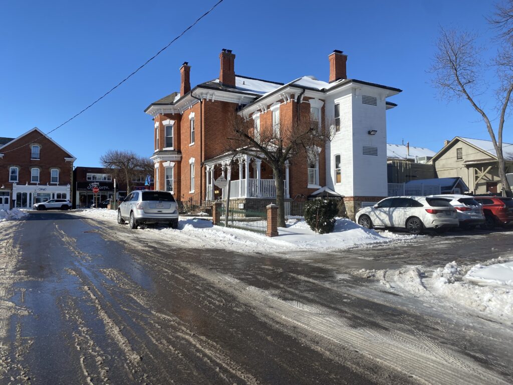 A slush-covered road leads to the parking lot behind an Italianate-style house.