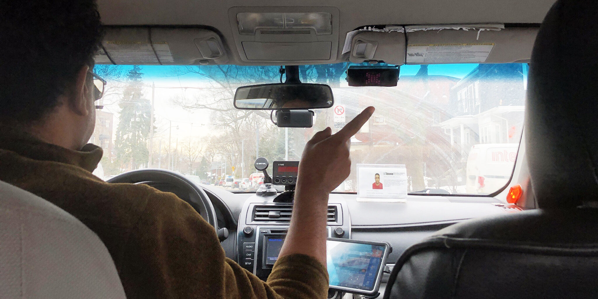 Rowan-Flood-Dick-Taxi-main Photo from the backseat of a taxi featuring the driver pointing out the window.