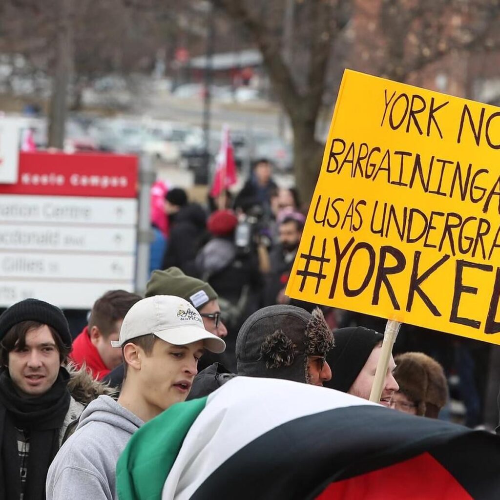Focus image of a protest filled with students, holding signs fighting for the rights of York University workers.