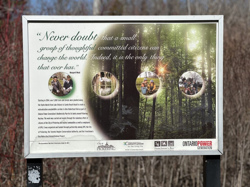 An informational sign sponsored by OPG. It has a quote in fancy lettering and a block of text beneath it. There is a semi-circle faded picture of trees visible on the right of the side, and four smaller circular pictures across the middle of the sign.