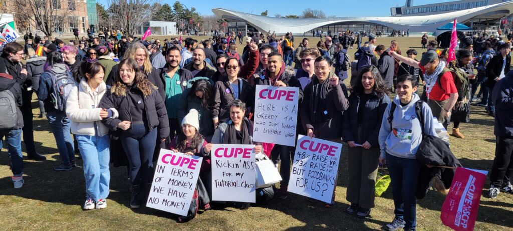Group of students and staff standing together holding "CUPE 3903" signs.