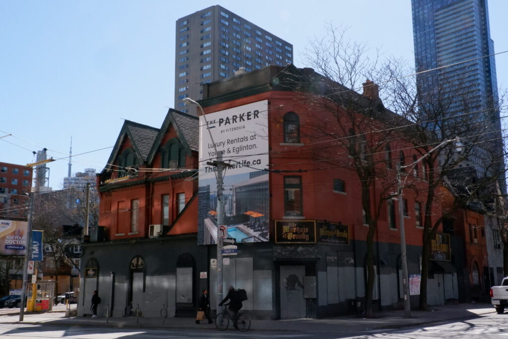 An old red brick building with boarded windows. A sign on the front of the building advertises a new condominium to be built