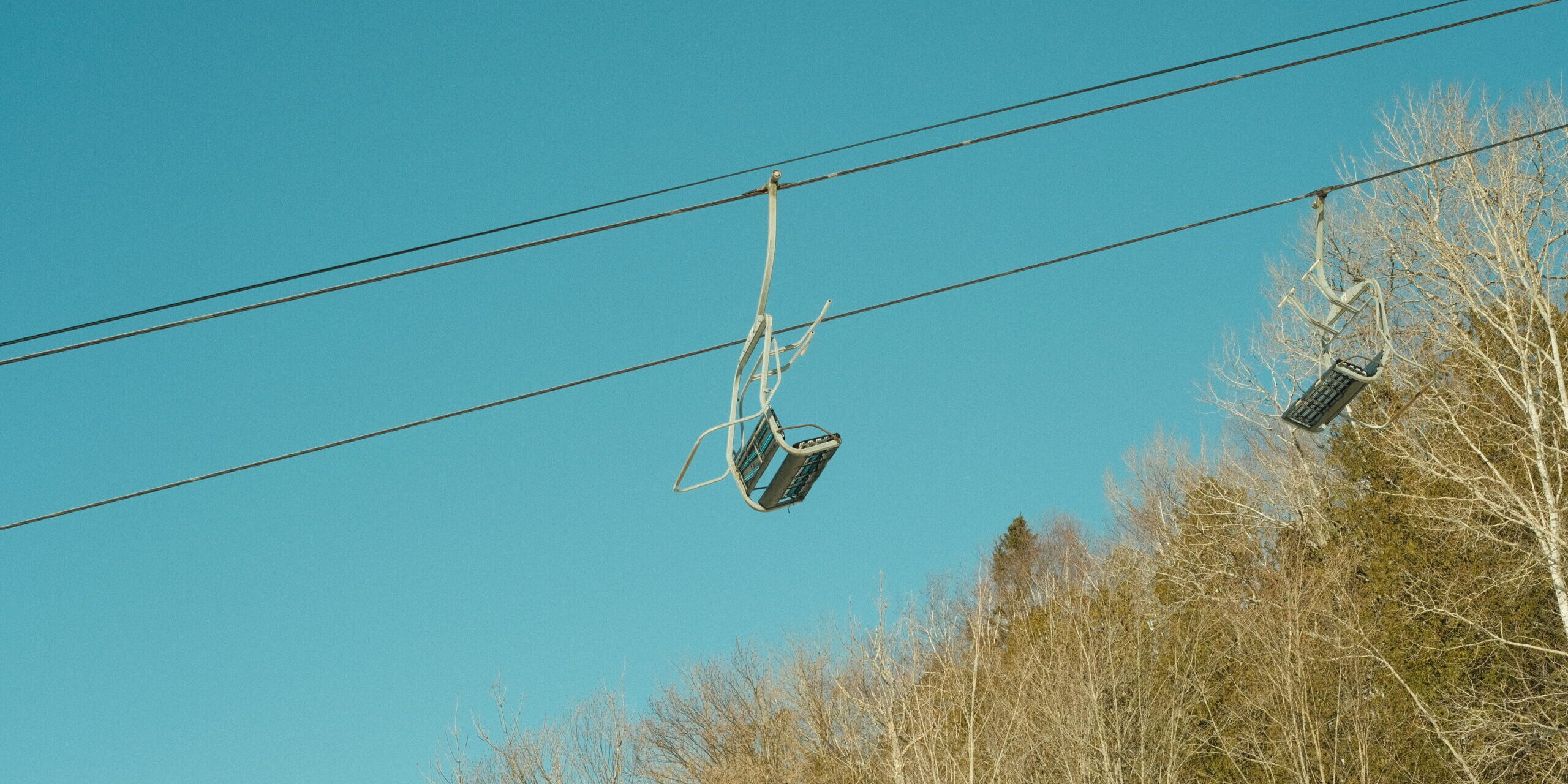 Header Photograph of ski lift chair with a blue sky and trees in the background.