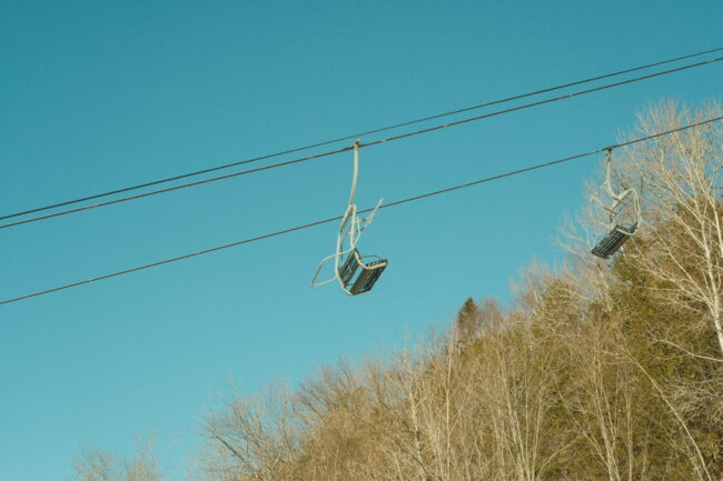 Header Photograph of ski lift chair with a blue sky and trees in the background.