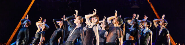 All That Jazz Still Kailin Brown as Velma in the musical Chicago. There are other people around them and they are in a pose from the number "All That Jazz" with their hand on their forehead. They are leaning towards the right side,