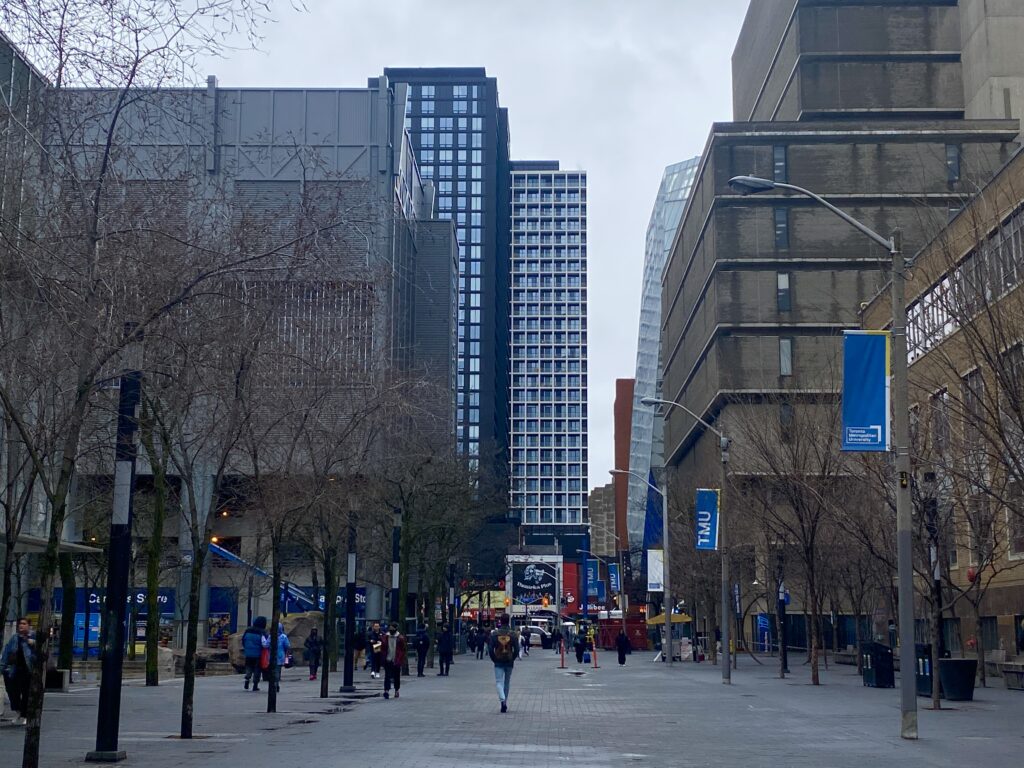 Students are walking on the Toronto Metropolitan University campus which is surrounded by tall buildings.
