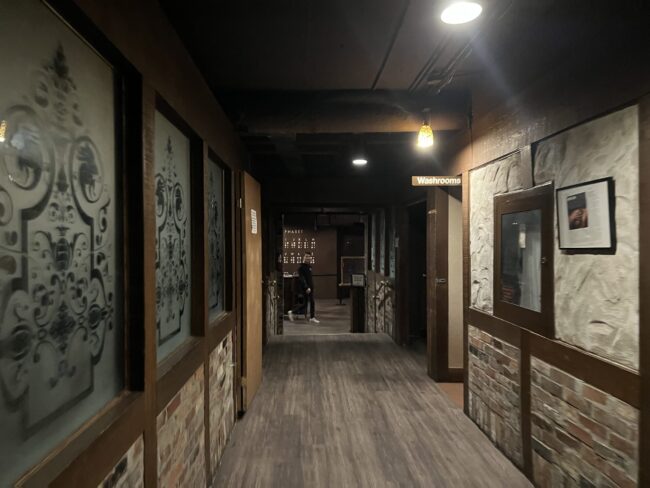 The photo shows the hallway when one enters O'Noir. The floor is grey-coloured hardwood panels and there is very dim lighting with brown wood and stone panelling on the walls.