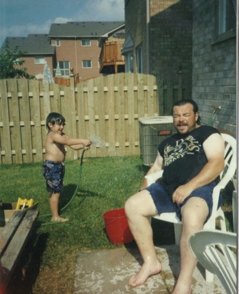 Young human boy spraying older human man with a hose.