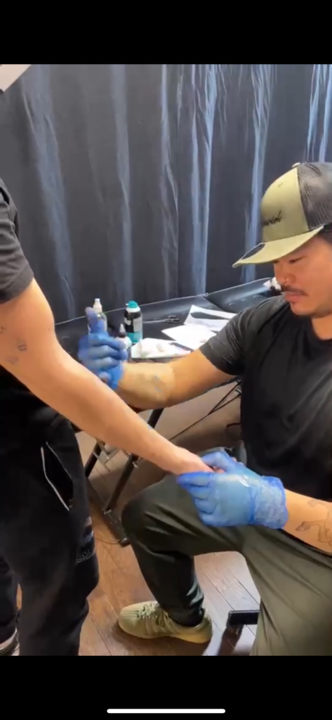 Image of Dela Cruz applying tattoo stencil to someones arm. 