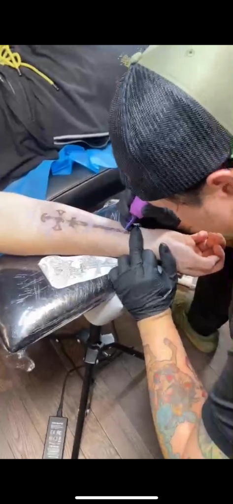 Image of Dela Cruz tattooing someone's arm. 