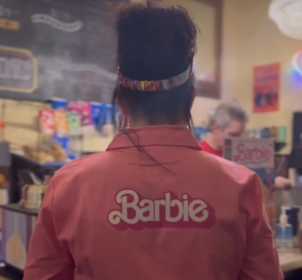 A person wearing a pink jumper with the Barbie logo.