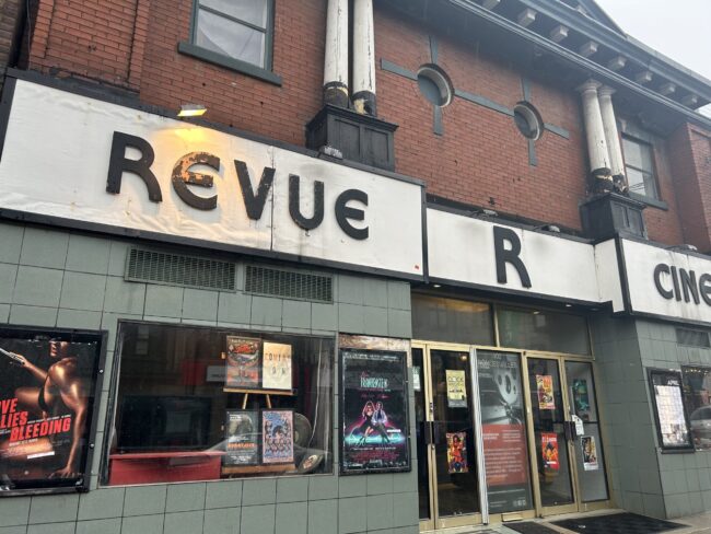 A green brick theatre with film posters on the front glass windows.