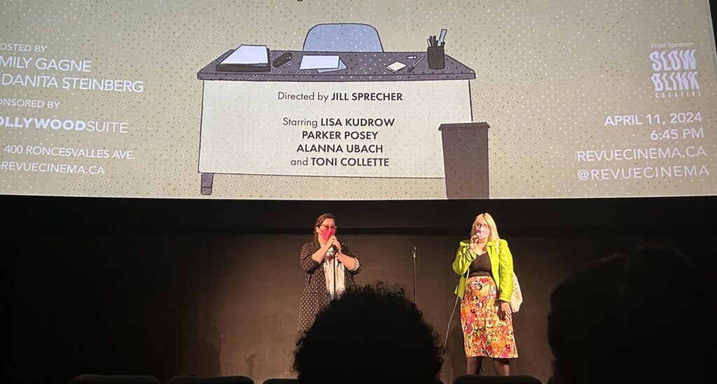 Two women holding microphones in front of a theatre screen.