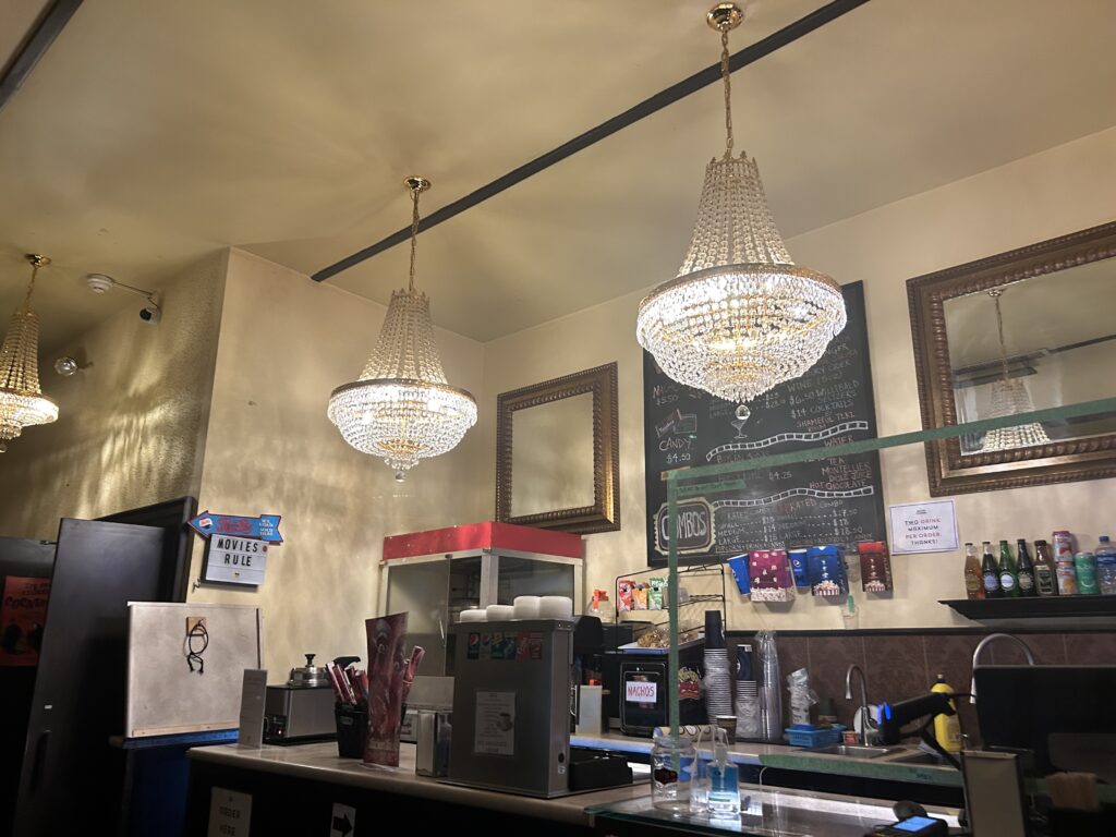 A movie theatre concession stand with two chandeliers hanging over it.