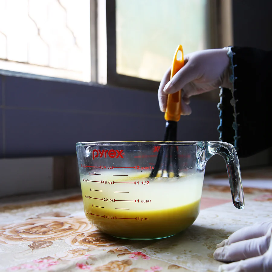 A refugee artisan woman whisking together soap ingredients in a measuring cup.