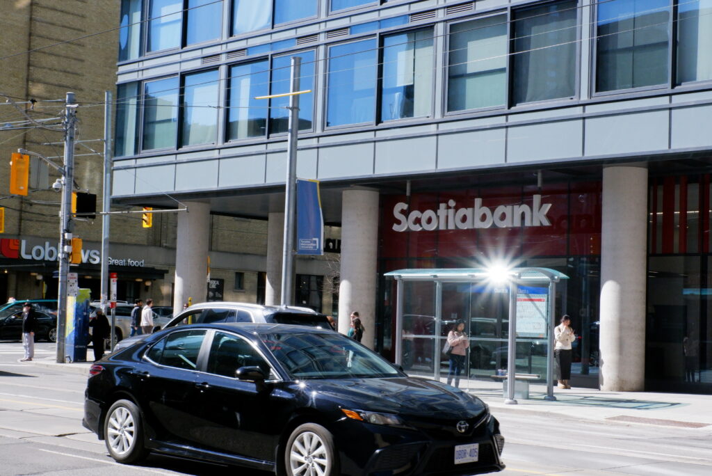 A black car parked outside of a Scotiabank situated at the bottom of a condo tower