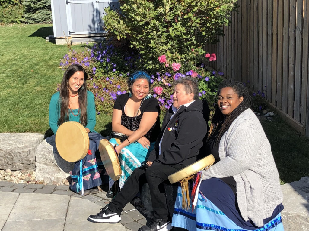 Members of Spirt Wind sitting on a rock holding traditional First Nations drum.