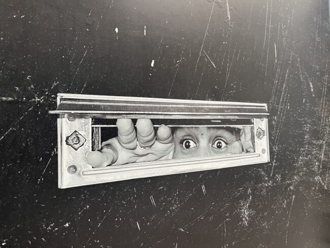 Black door with an image of eyes peeking out of a mail slot