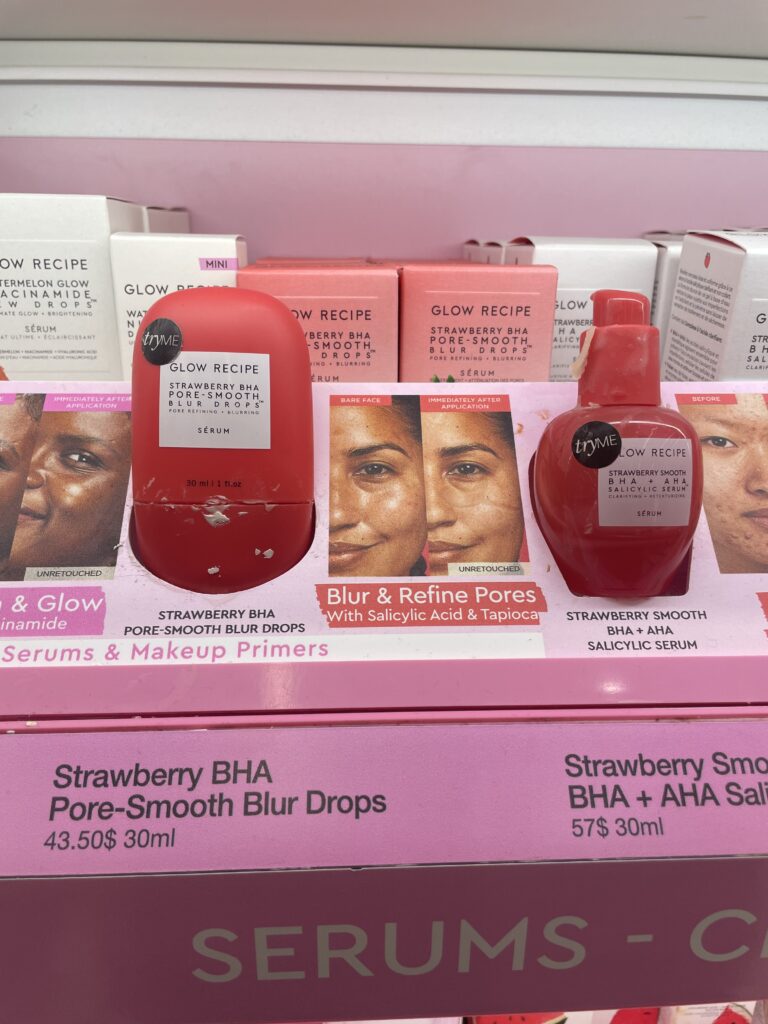 Two fuchsia pink skincare bottles on a light pink display with product stains.