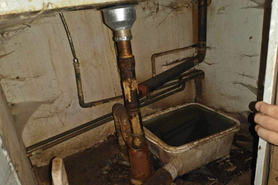 Rusty old pipes in a kitchen sink base cabinet.