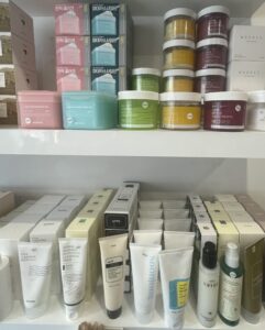 A white shelf with colourful jars of toner pads on the top-level of the shelf and some cleansers on the bottom-level of the shelf.