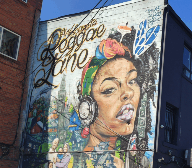 Photo of a wall mural, with a black female next to the text "Reggae Lane"